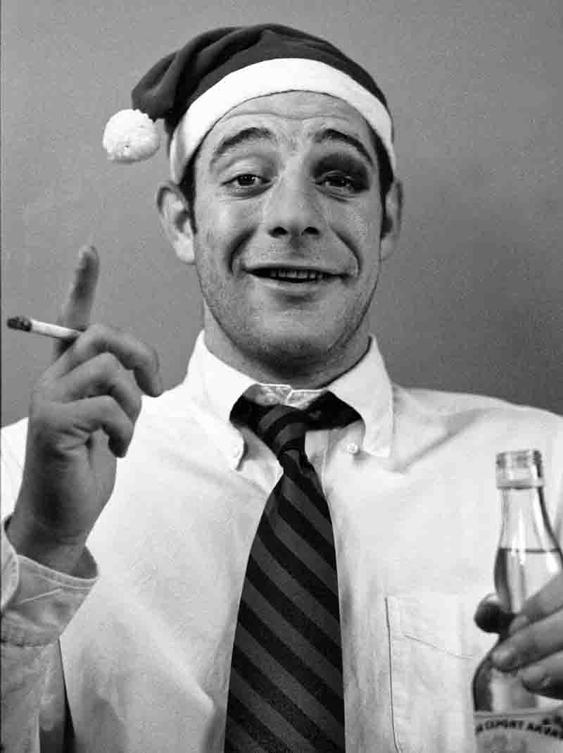 A man wearing a Santa hat smokes a cigarette while holding a vodka bottle, embodying a festive yet relaxed atmosphere.