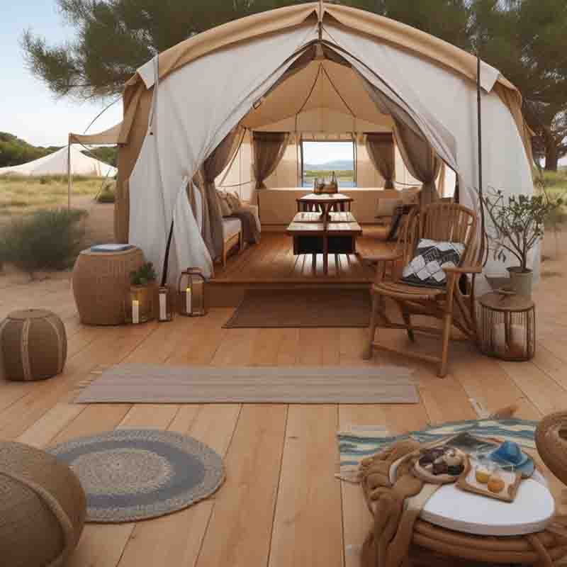 Serene glamping scene set in Ibiza. The centerpiece is a white tent, which stands on a wooden deck. The tent is furnished with a wooden table and chairs, a bench, and a side table, creating a cozy and inviting space.