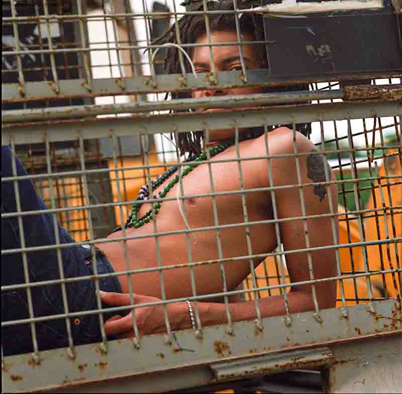 Portrait photography of a man sitting inside a cage, looking out with a somber expression.