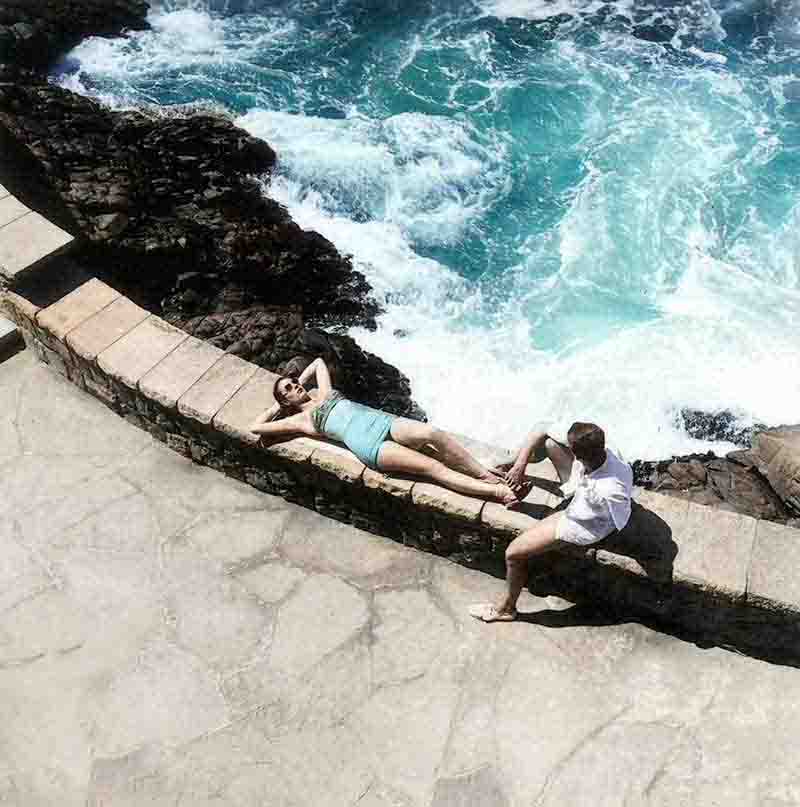 A couple enjoying a serene moment on a ledge overlooking the ocean.