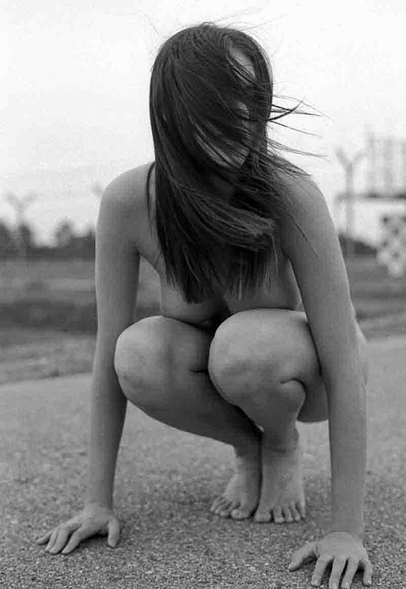 A woman crouching on the ground, unclothed.