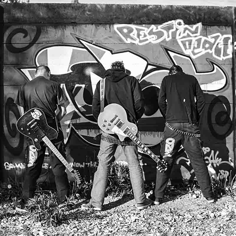 Three Musicians with their guitars facing a graffity painted wall