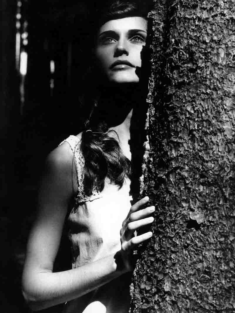 Fashion Model leaning against a tree in the woods, enjoying the serene beauty of nature.